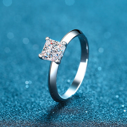 A princess cut solitaire moissanite diamond ring with a chevron pattern on a blue, sparkly background.
